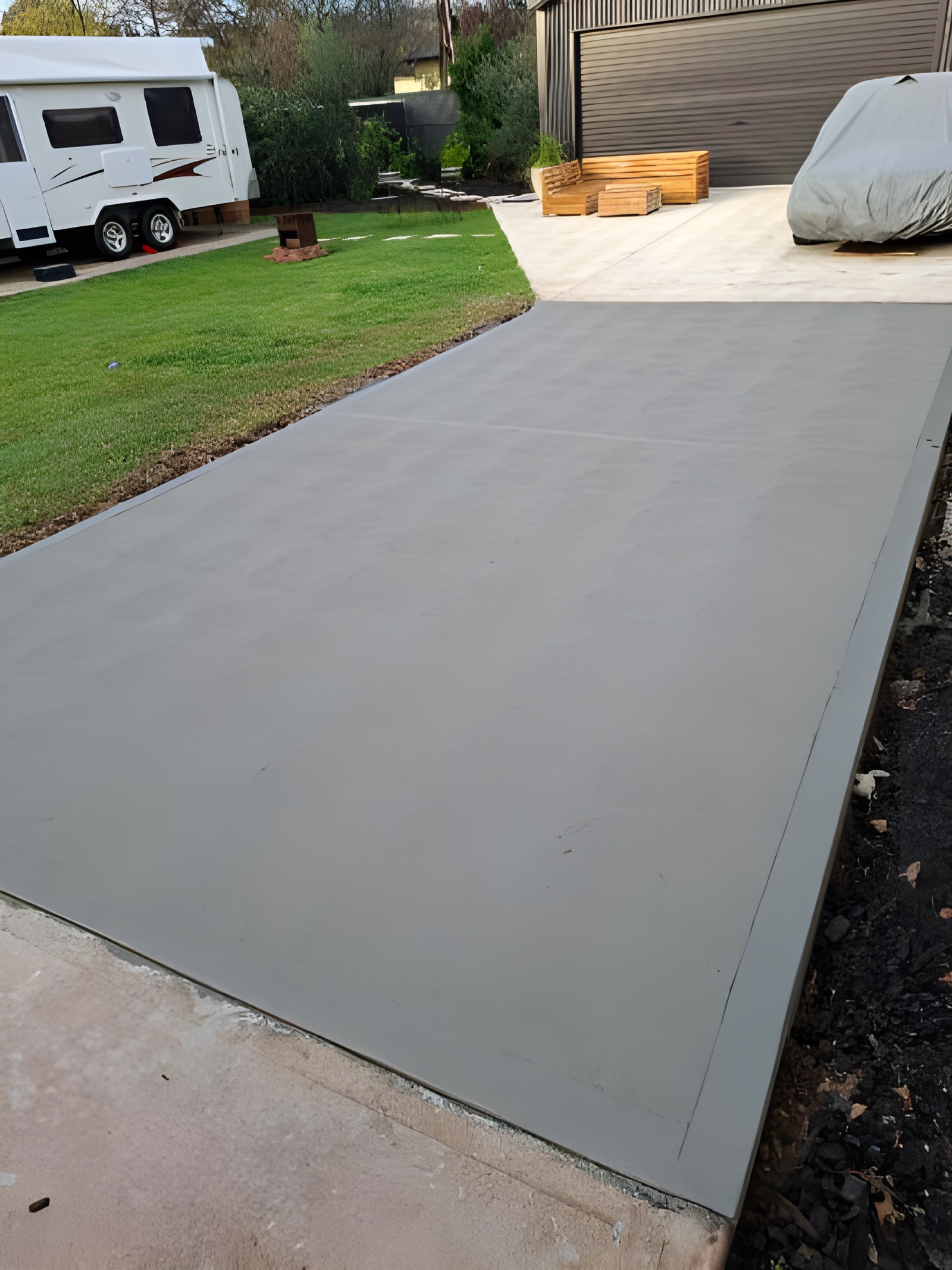 Large freshly set concrete caravan pad and driveway slab beside a lawn