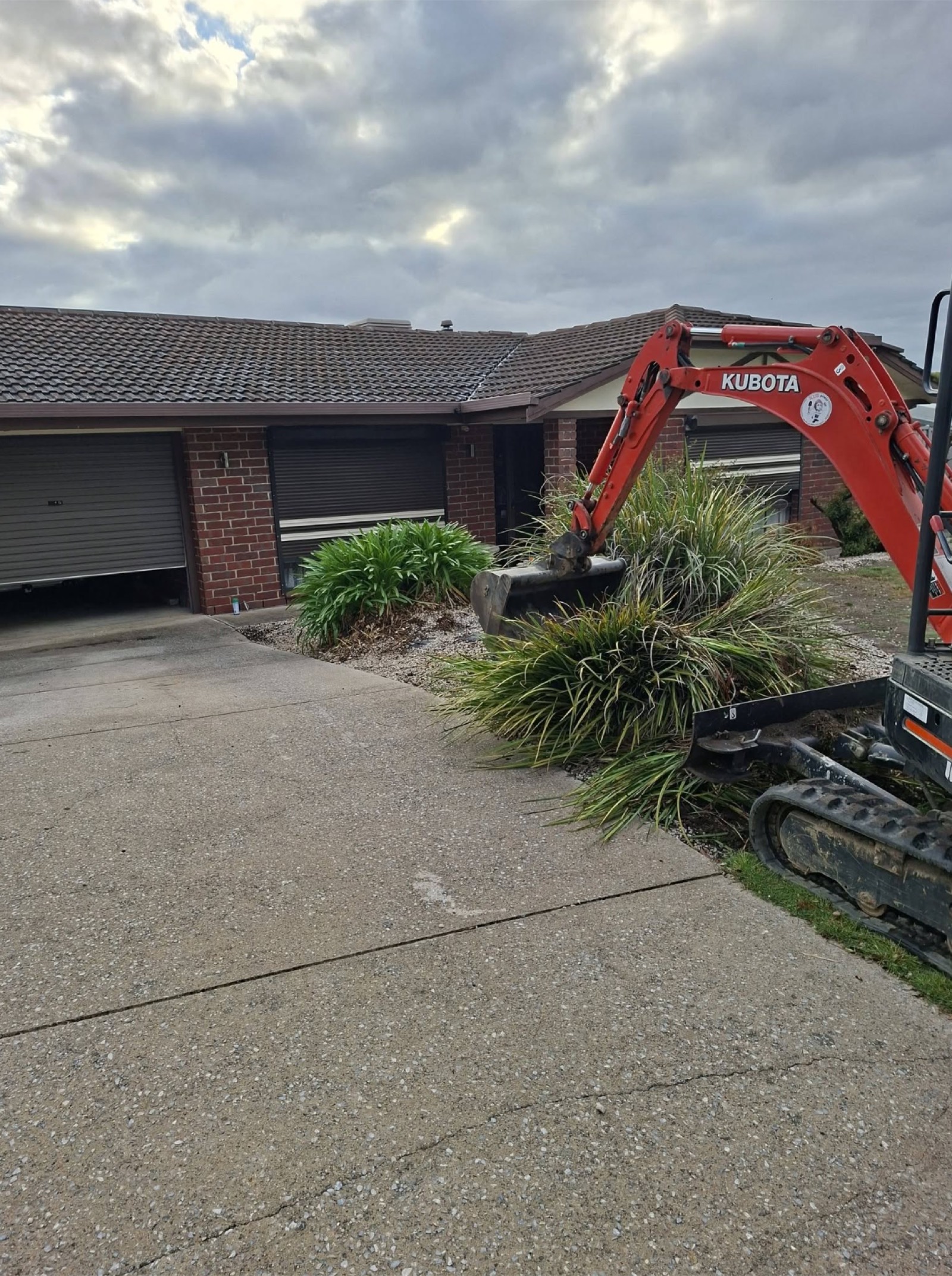 Mini excavator clearing a front garden bed ahead of a new driveway pour